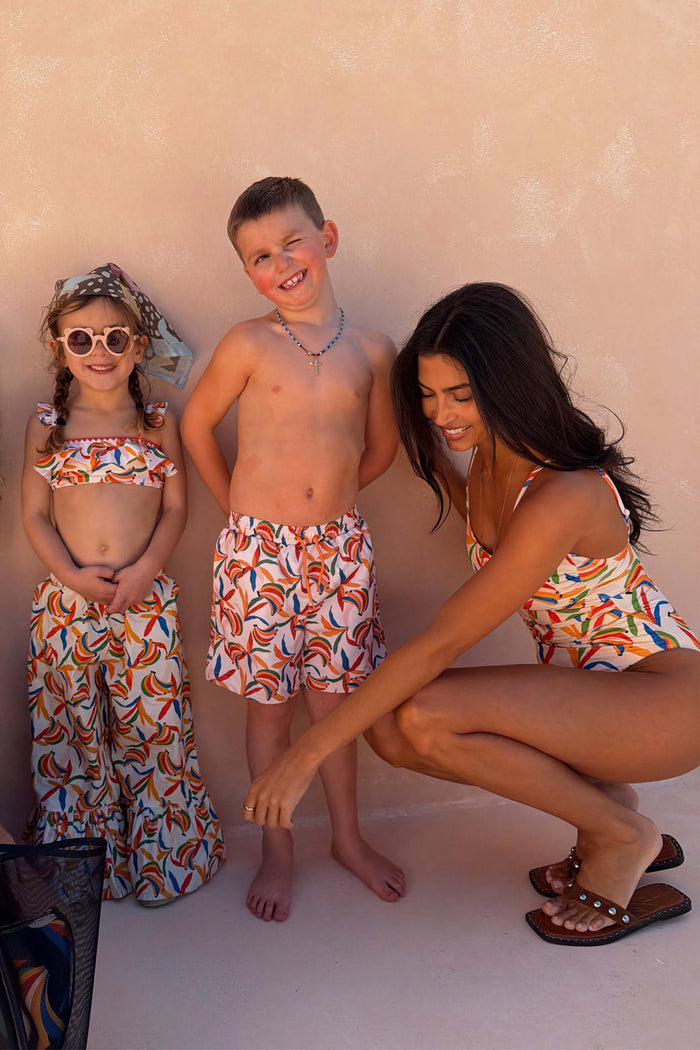 Boy's Banana Print Swim Shorts in cream with multi-coloured fruit, styled with matching family vacation swimwear.