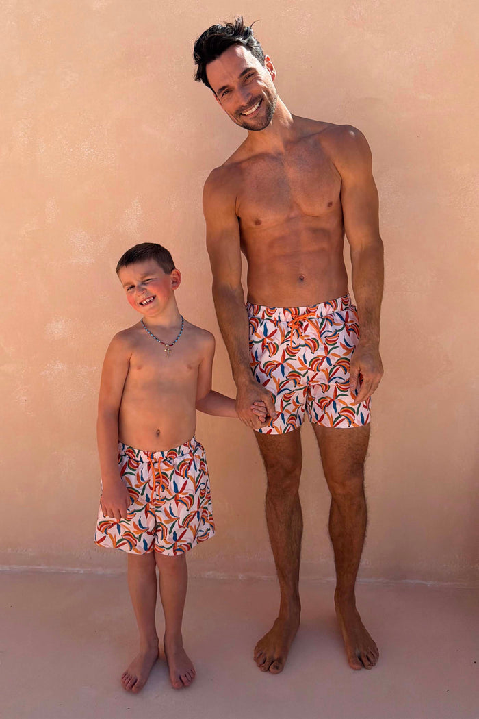 Matching banana print swim shorts in cream with orange drawstrings on a man and boy for a family vacation look.