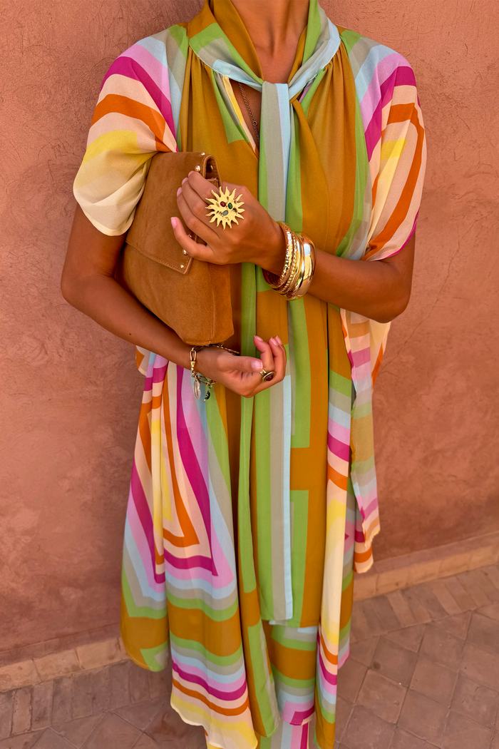 Bright Geo Stevie Maxi Dress featuring colourful geometric stripes and a scarf-tie neck, styled with a tan suede clutch.