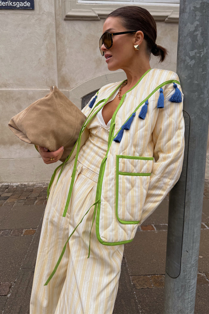 Butter Yellow Stripe Quilted Jacket with green trim and blue tassels, worn by a model in an outdoor street setting.