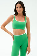 A woman models the SPLITS59 Cait Rigor Bra in Grass/White, paired with matching high-waisted leggings featuring white trim—ideal for high-impact workouts—against a plain light background.