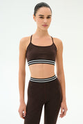 A person stands facing forward, wearing the SPLITS59 Cali Active Rib Bra in Heather Dark Chocolate and matching high-waisted leggings with black and white striped bands.