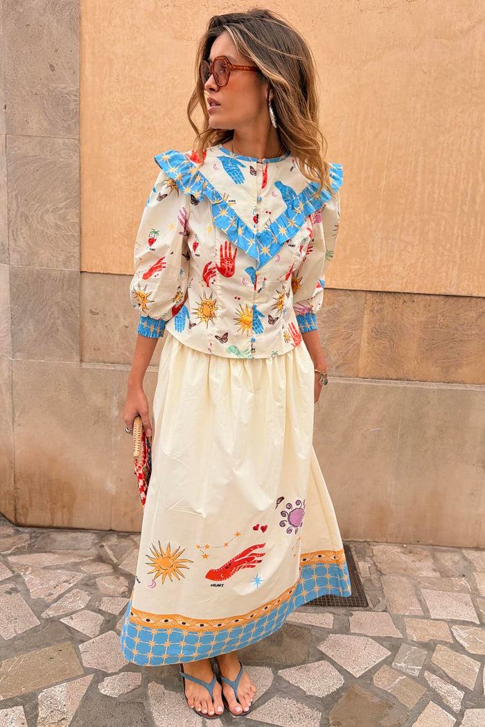 Cream cotton Celestial Nia Top featuring a celestial sun print, blue ruffled shoulders and button-up front.