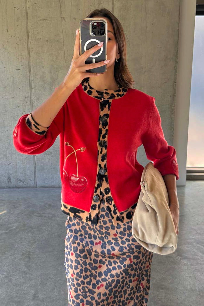 Red knit Cherry Holly Cardigan with wide sleeves, leopard print trim and cherry motifs, over a leopard skirt.