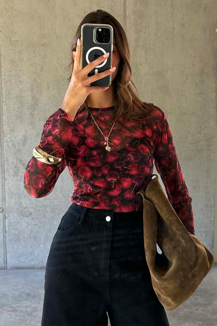Cherry Mesh Long Sleeve Top with a red cherry print and sheer finish, designed in the UK and styled with black trousers.