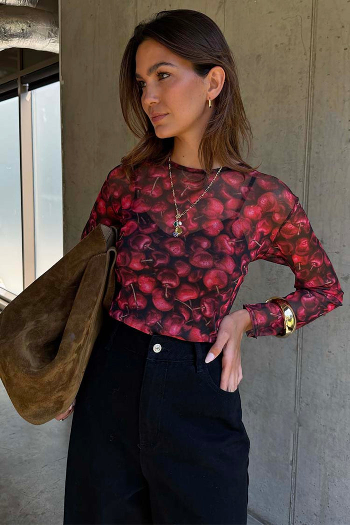 Cherry Mesh Long Sleeve Top in red sheer mesh with a cherry print, paired with black trousers and a brown bag.