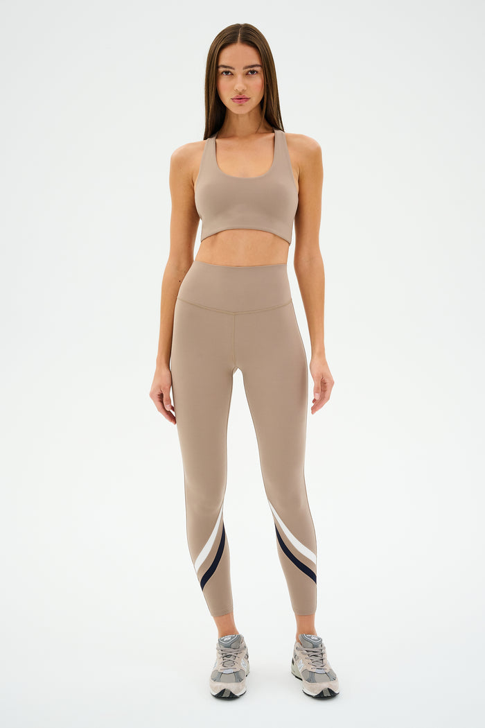 A person wearing SPLITS59's Chevron Airweight High Waist 7/8 leggings in Latte/Indigo and an ultra-luxe fabric sports bra stands on a white background.