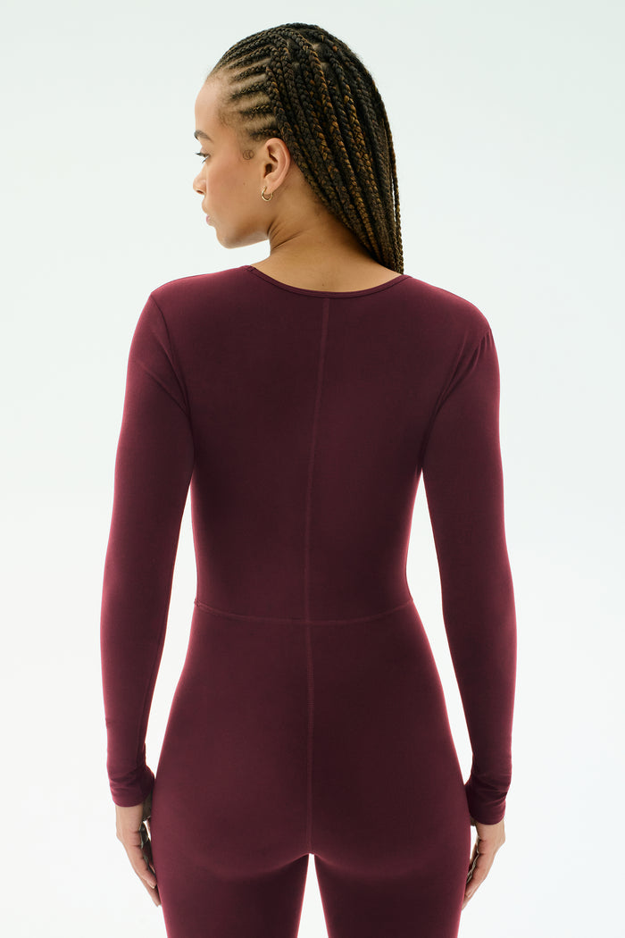 A person with braided hair models the SPLITS59 Chloe Airweight Jumpsuit in Dark Cherry, standing with their back to the camera against a plain light background.