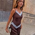 Chocolate Aurelia Top in brown satin with blue lace trim, V-neckline and pointed hem, styled outdoors.
