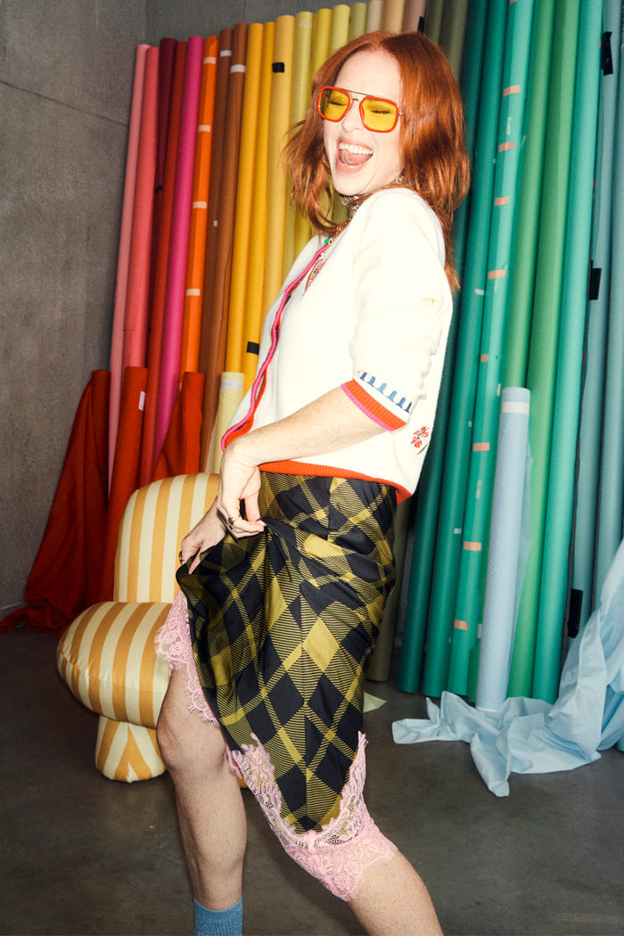 White Choose Love Cardigan with colourful trims and a chequered skirt on Angela Scanlon in a studio setting.