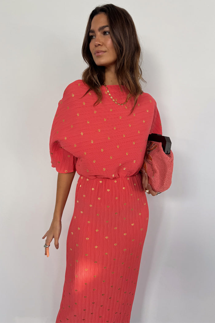 Coral Plisse Tilly Dress featuring gold flecks, an off-the-shoulder neckline and elasticated waist, styled with a pink clutch.