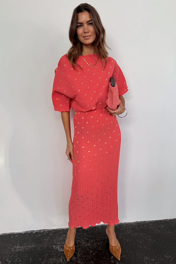Coral Plisse Tilly Dress with gold flecks, wide draped sleeves and a lettuce hem, styled with a pink clutch bag.
