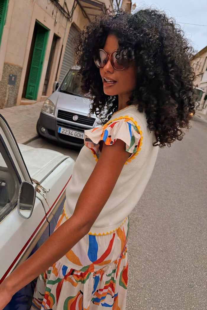Cream knit Banana Tank with yellow contrast stitching, layered over a colourful abstract print skirt on a city street.