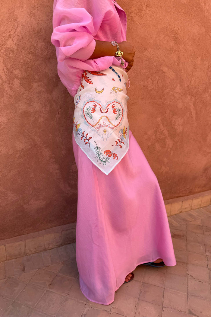 Cream Bandana in Tigress Print with a floral heart motif, tied around the waist over a pink maxi skirt.