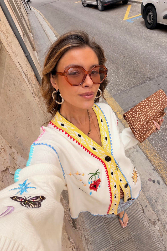 Cream Celestial Martha Cardigan in a soft touch knit with colourful embroidery and yellow trim, styled on a city street.