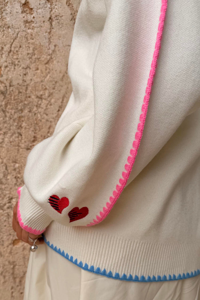 Cream Celestial Martha Cardigan detail highlighting the pink scalloped trim, red hearts and blue contrast hem.