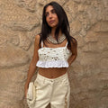 Cream Mirror Gabbi Top with mirror embellishments and a ruffle hem, styled with trousers against a stone wall.
