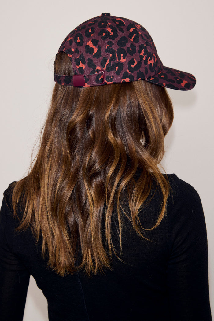 Dark Leopard Cap in iconic burgundy leopard print with adjustable back strap, shown on a model.