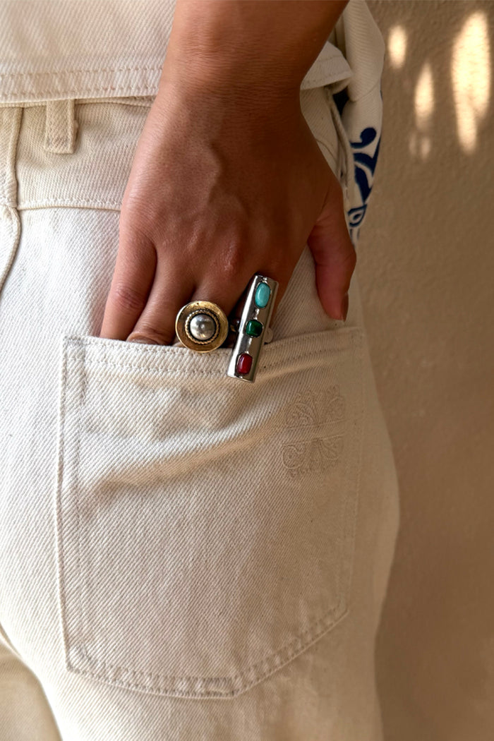 Deloris Whistle Ring with turquoise, green and red gemstones on a chunky silver-toned band, styled on a hand in a pocket.