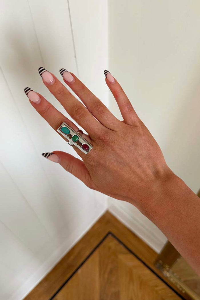 Chunky Deloris Whistle Ring with teal, green and red gemstones, styled on a hand with striped nail art.