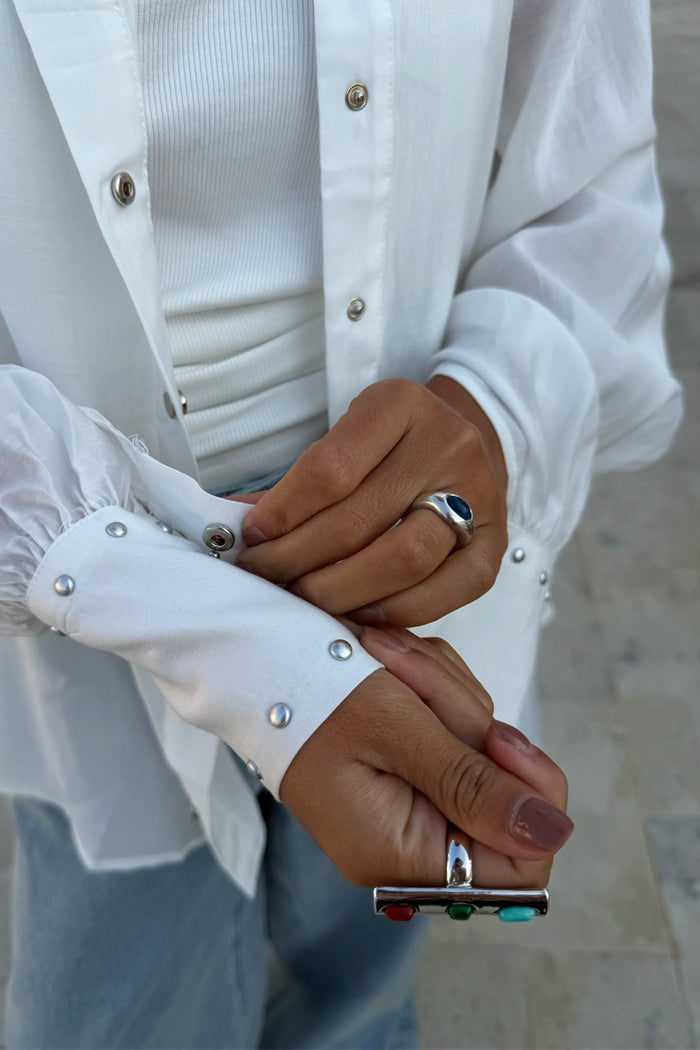 Chunky Deloris Whistle Ring with red, green and turquoise gemstones, styled on a model in a white studded shirt.