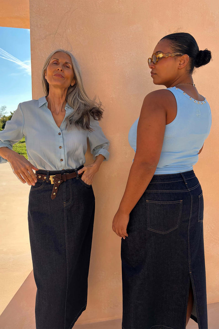 Dark blue denim midi pencil skirt with a back slit, shown on two models to highlight inclusive sizing.