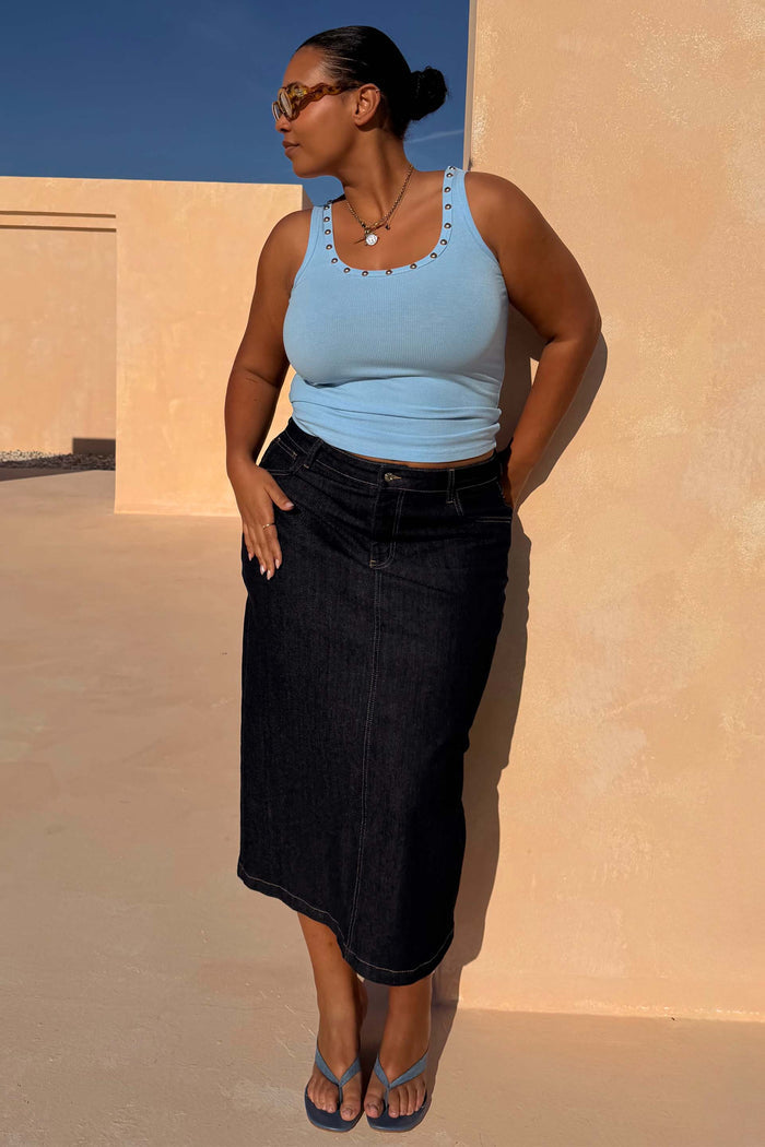 Dark blue denim pencil midi skirt and light blue eyelet vest, designed in London and showcasing inclusive sizing.