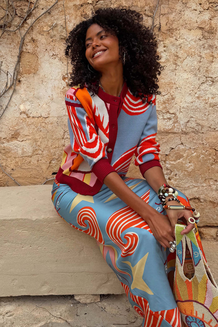 Dolce Vita Hollie Cardigan with eye graphics and swirl motifs, styled on a model sitting against a stone wall.