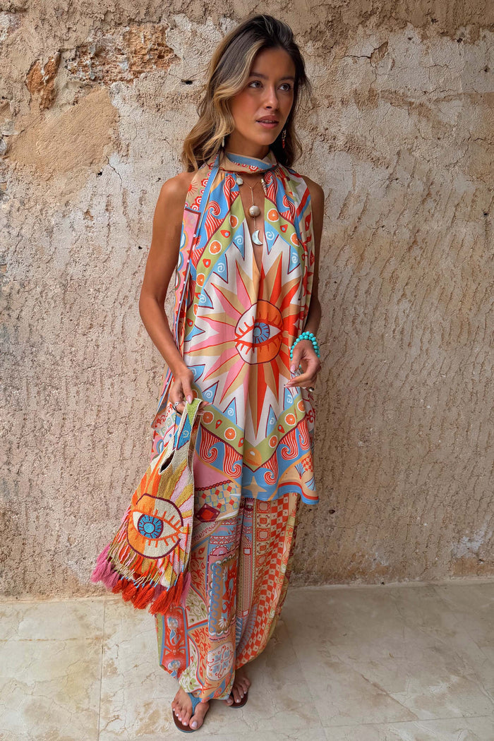 Dolce Vita Josie Mini Dress with iconic eye motif and scarf neck, styled over matching sunset tone trousers.