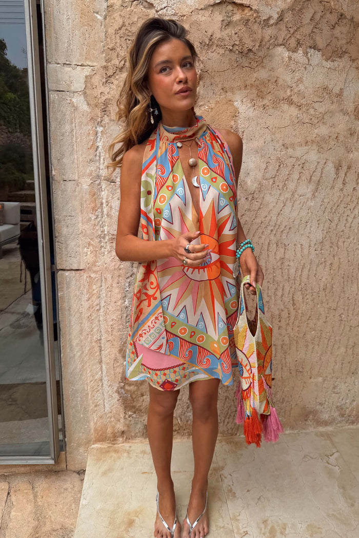Dolce Vita Josie Mini Dress in sunset tones featuring an iconic eye motif and scarf halterneck.