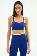 A woman poses against a plain background in the SPLITS59 Elliah Airweight Double Layer Bra in cobalt/white, styled with matching high-waisted leggings featuring white trim.