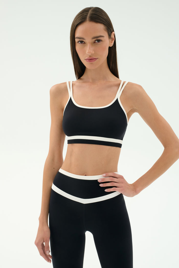 A woman faces forward against a plain light background, wearing the SPLITS59 Eva Rigor Double Strap Bra in black/white and matching leggings.