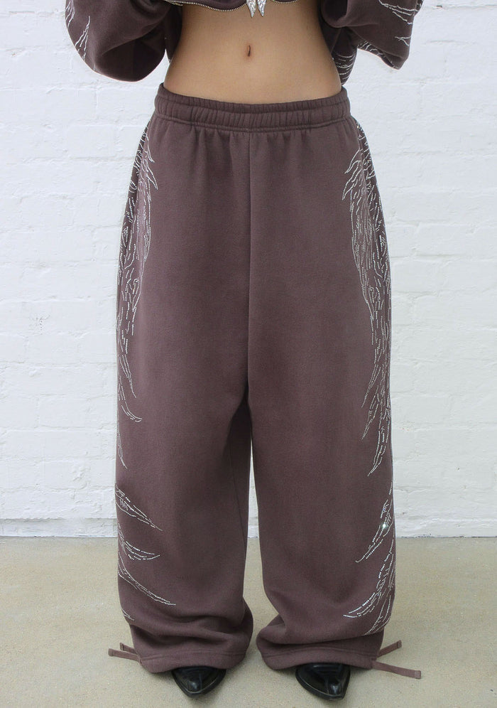 Front view of brown sweatpants featuring rhinestone wing design and adjustable ankle ties.