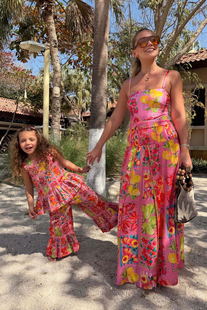 NFD Kids Pink Fruit Wide Leg Set with a cotton peplum top and frill hems on a child posing on a sandy beach vacation.