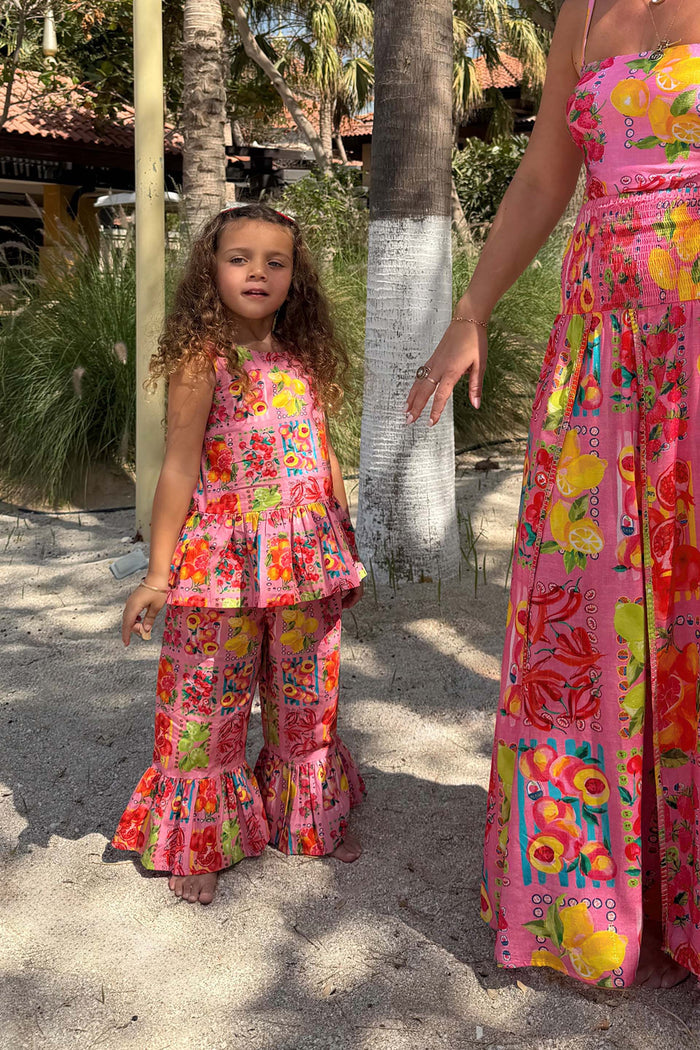 Pink Fruit Wide Leg Set with a Mediterranean print, peplum top and frilled trousers on a girl during a beach vacation.