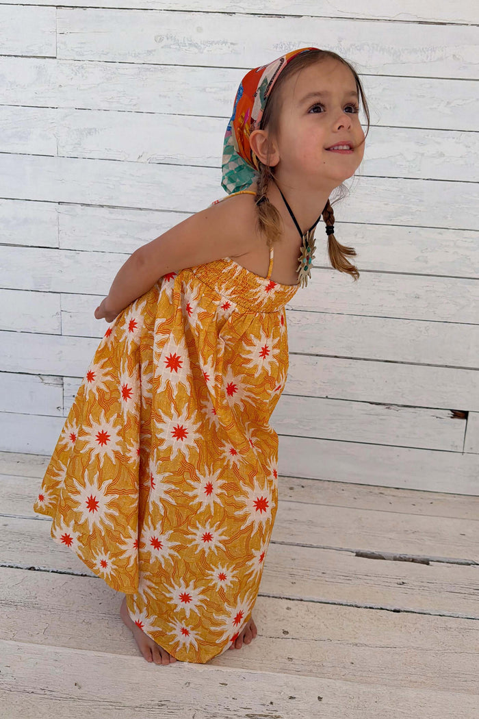 NFD Kids yellow cotton maxi sun dress with a vibrant sun print and shirred top, worn by a young girl.