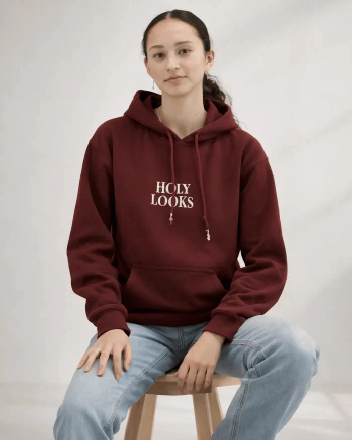 Person wearing a maroon hoodie with 'HOLY LOOKS' text, sitting on a stool against a plain background