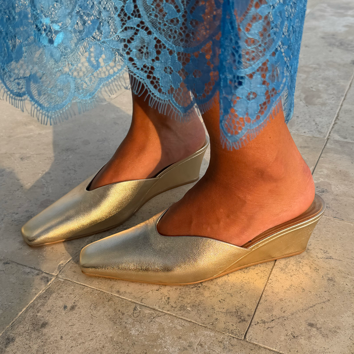 Metallic Gold Wedge Mule heels with a pointed toe and sculpted heel, styled with a blue lace dress.