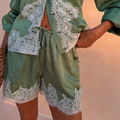 Green satin Maeva Shorts with white lace trim and a drawstring waist, styled with a matching lace-trimmed shirt.