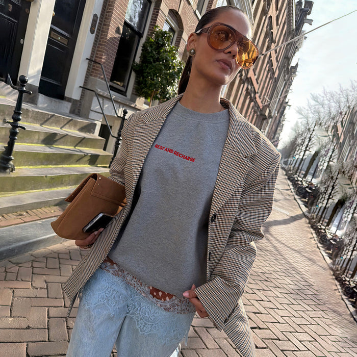 Grey Rest and Recharge Jumper with red lettering, layered with a checked blazer and lace-trim denim for a London look.