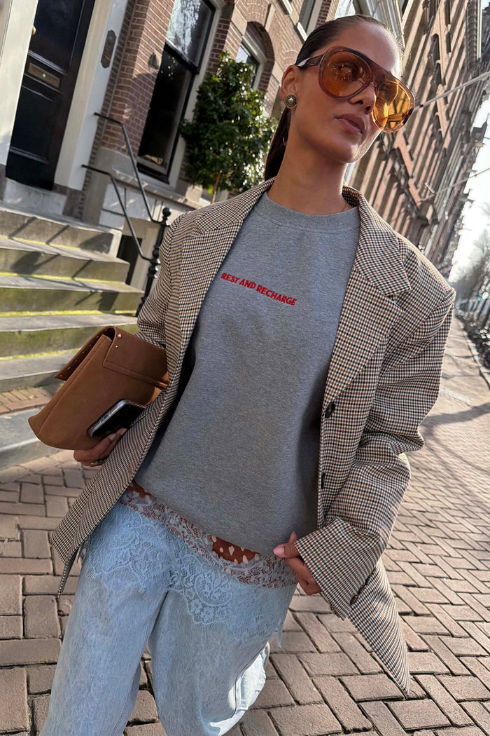 Grey Rest and Recharge Jumper with red text, layered under a check blazer for a London street style look.