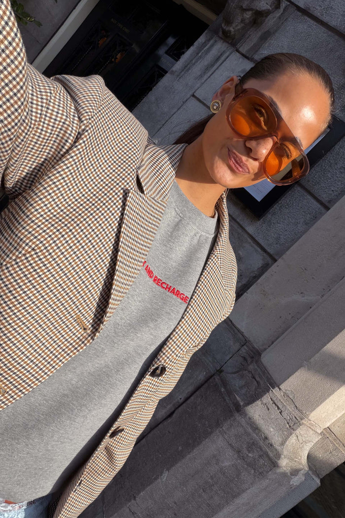 Grey Rest and Recharge Jumper with red lettering, layered under a check blazer for a versatile London look.