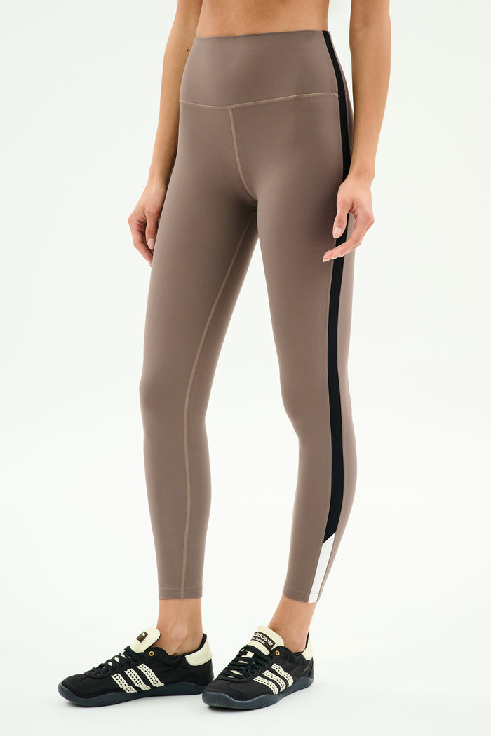 Model wears SPLITS59 Layla Airweight High Waist 7/8 leggings in Lentil/Black, showcasing ultra-soft fabric and black side stripe with black athletic shoes—ideal for hot yoga or daily wear, set against a plain white background.