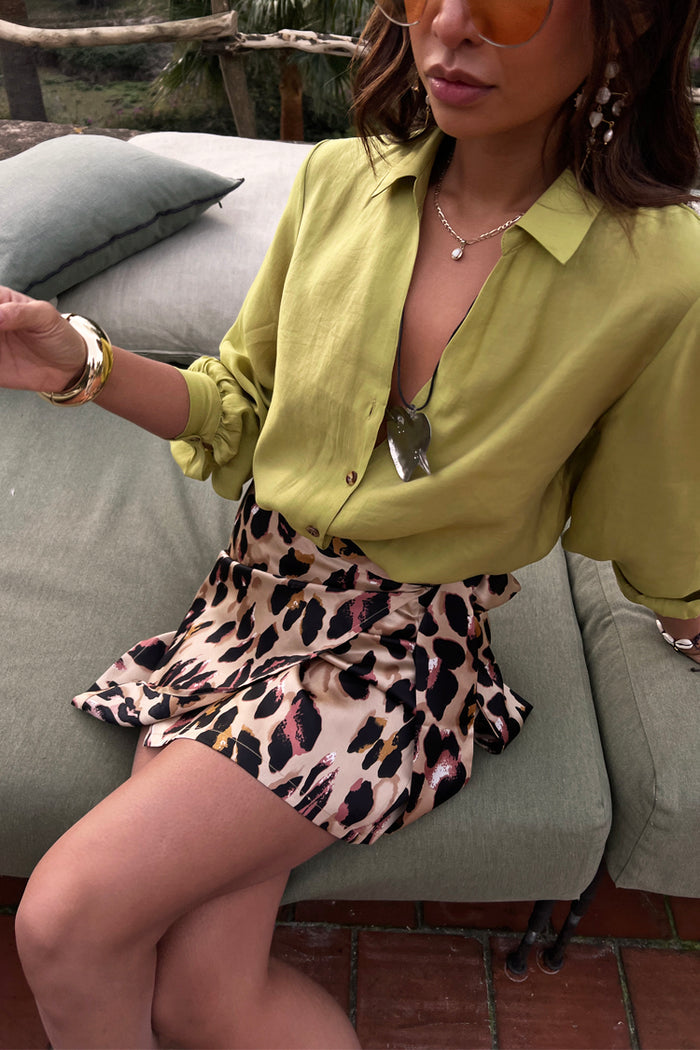 Model wearing a leopard mini Jaspre wrap skirt and lime green shirt while sitting outdoors.