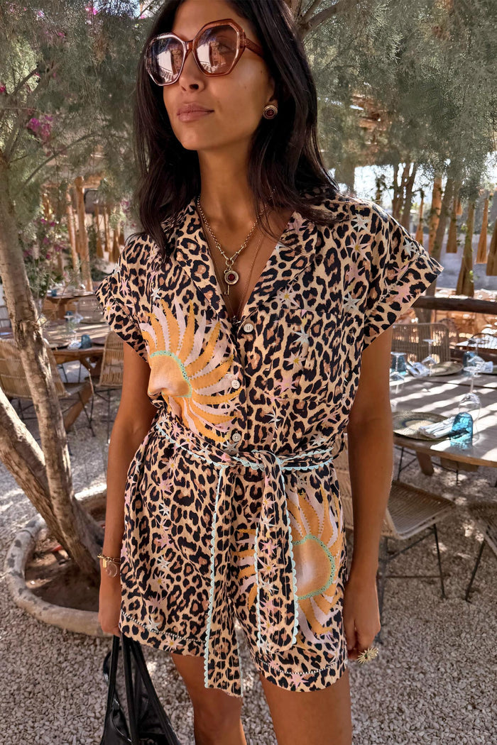 Leopard Print Playsuit with soleil motifs, turquoise trim and a tie waist, worn by a model at an outdoor cafe.