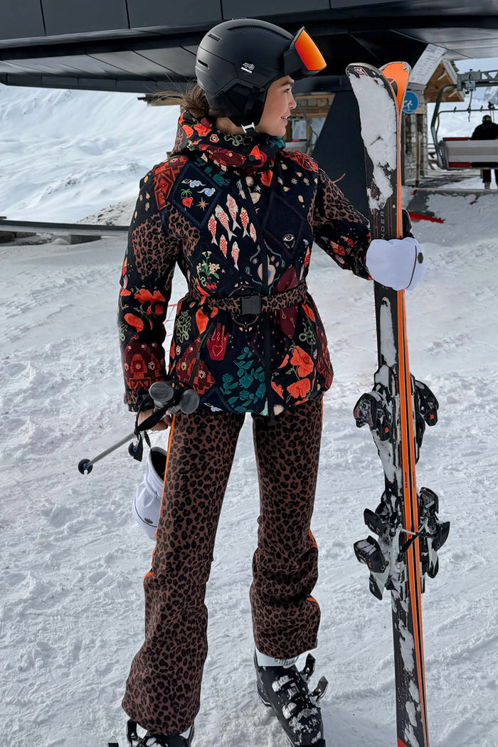 Leopard Ski Trousers paired with a patterned ski jacket, shown on a model with skis in a snowy landscape.