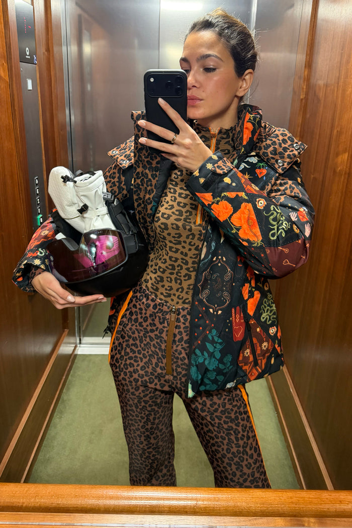 Leopard Ski Trousers with a high waist and orange side stripes, styled with a matching leopard top and ski gear.