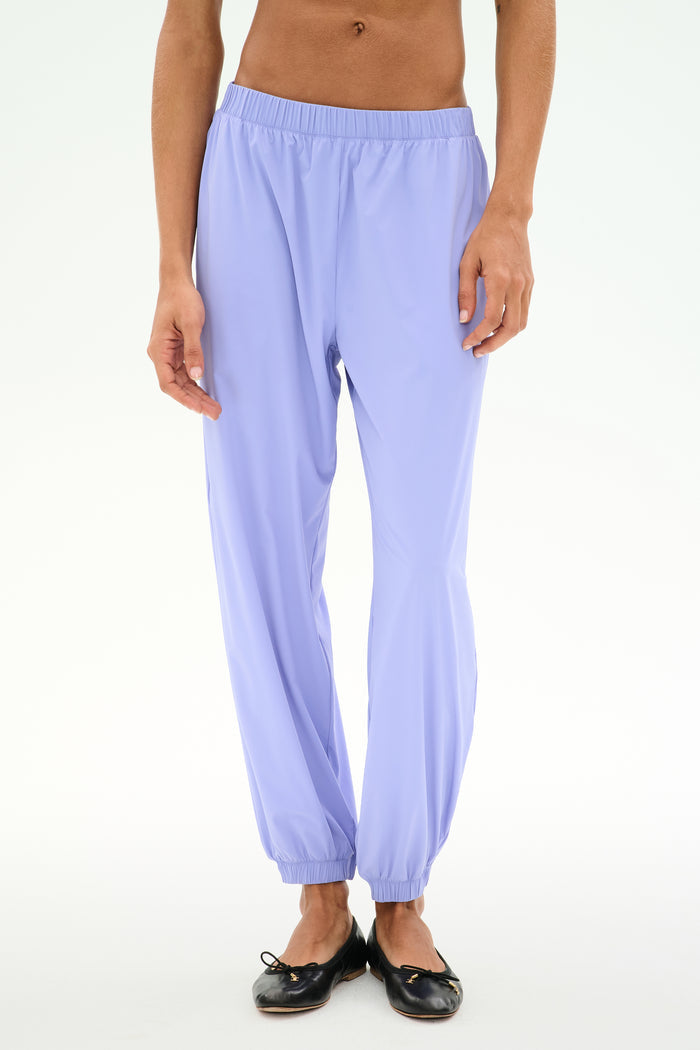 A person wearing SPLITS59's Megan Woven Nylon Jogger in Purple Haze with black ballet flats stands against a plain white background.