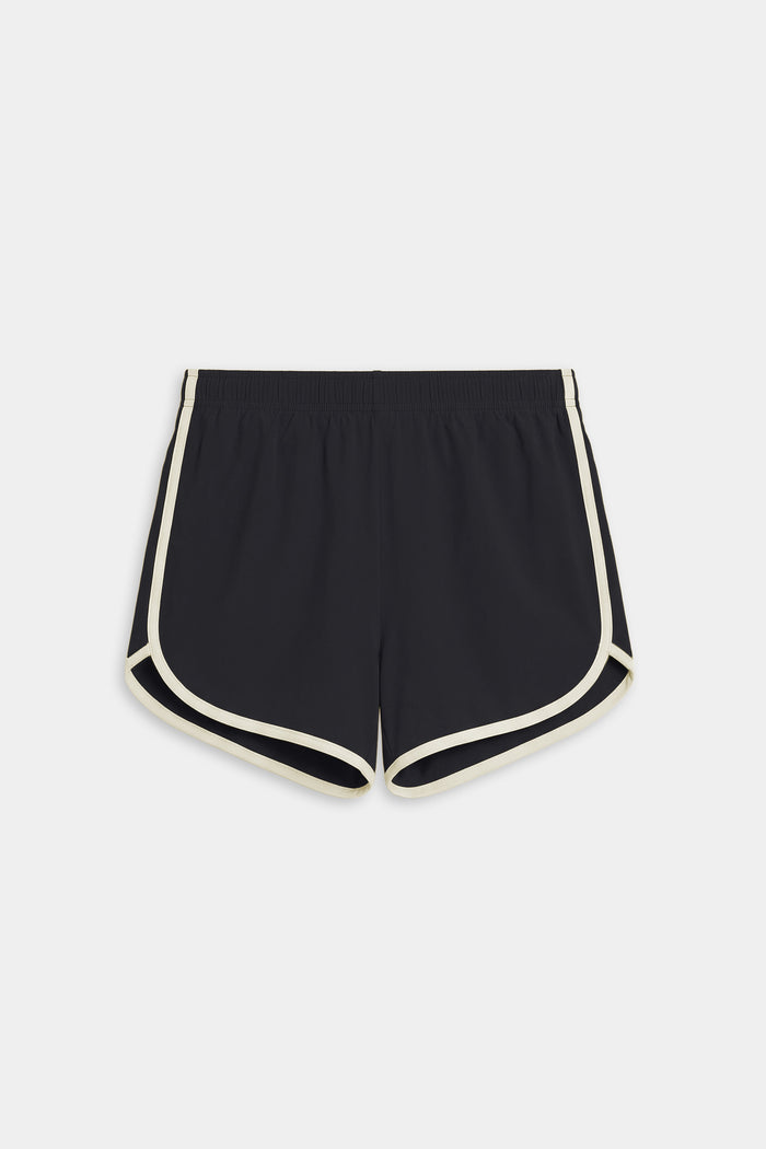 The SPLITS59 Megan Woven Nylon Run Short in Black/Creme features white trim, an elastic waistband, and curved hems in a nylon-spandex blend, shown laid flat on a white background.