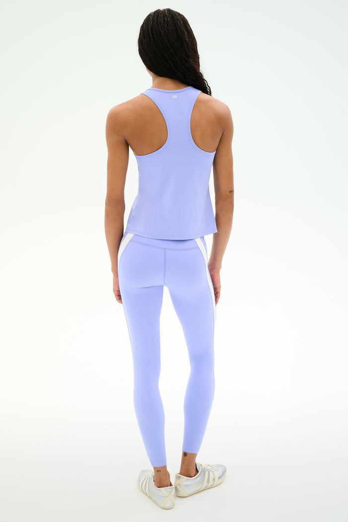 A person faces away, wearing the SPLITS59 Mel Airweight Lite Tank in Purple Haze with matching leggings and white sneakers, set against a plain white background.